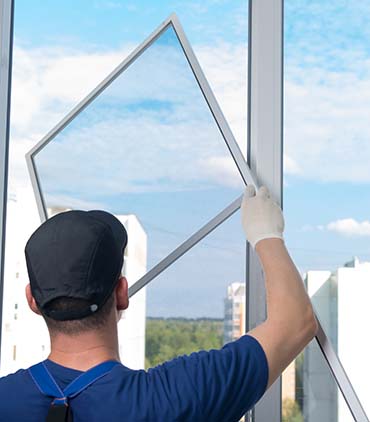 a worker in a blue uniform, rear view, installs a mosquito net in a plastic window frame, against the sky